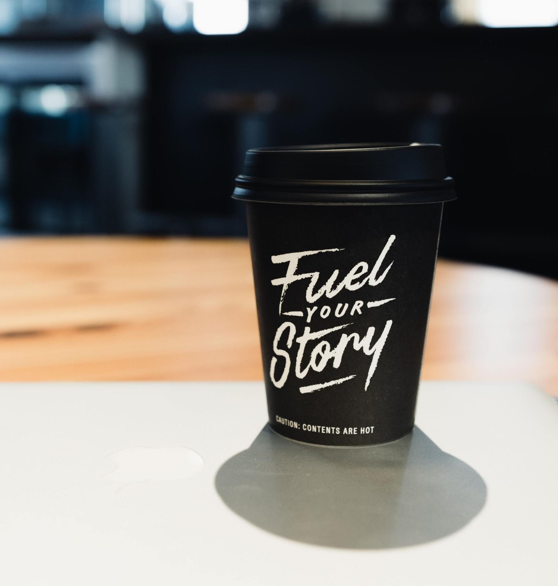 A cup of coffee with the words `` fuel your story '' written on it is sitting on a table.