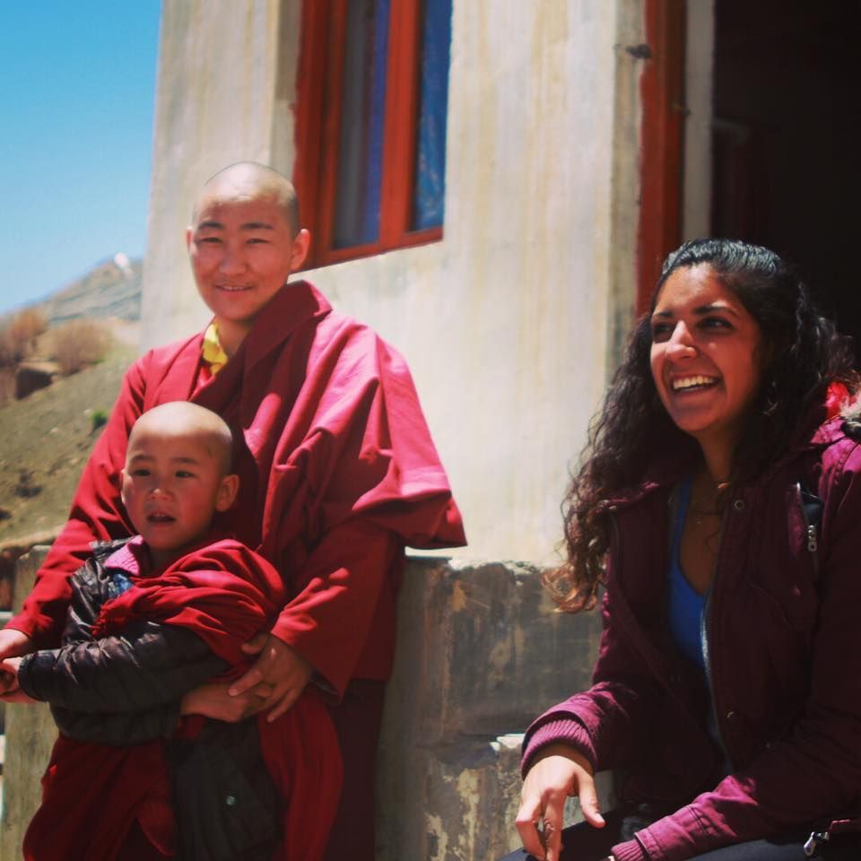 Two people and a child in red robes smiling outside a building in bright sunlight
