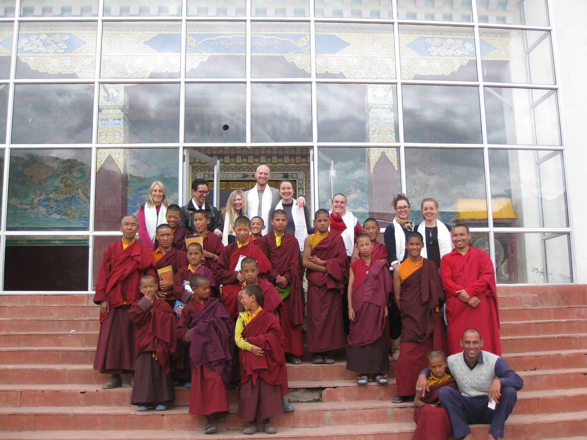 Group of people in maroon robes posing on steps outside a glass-fronted building