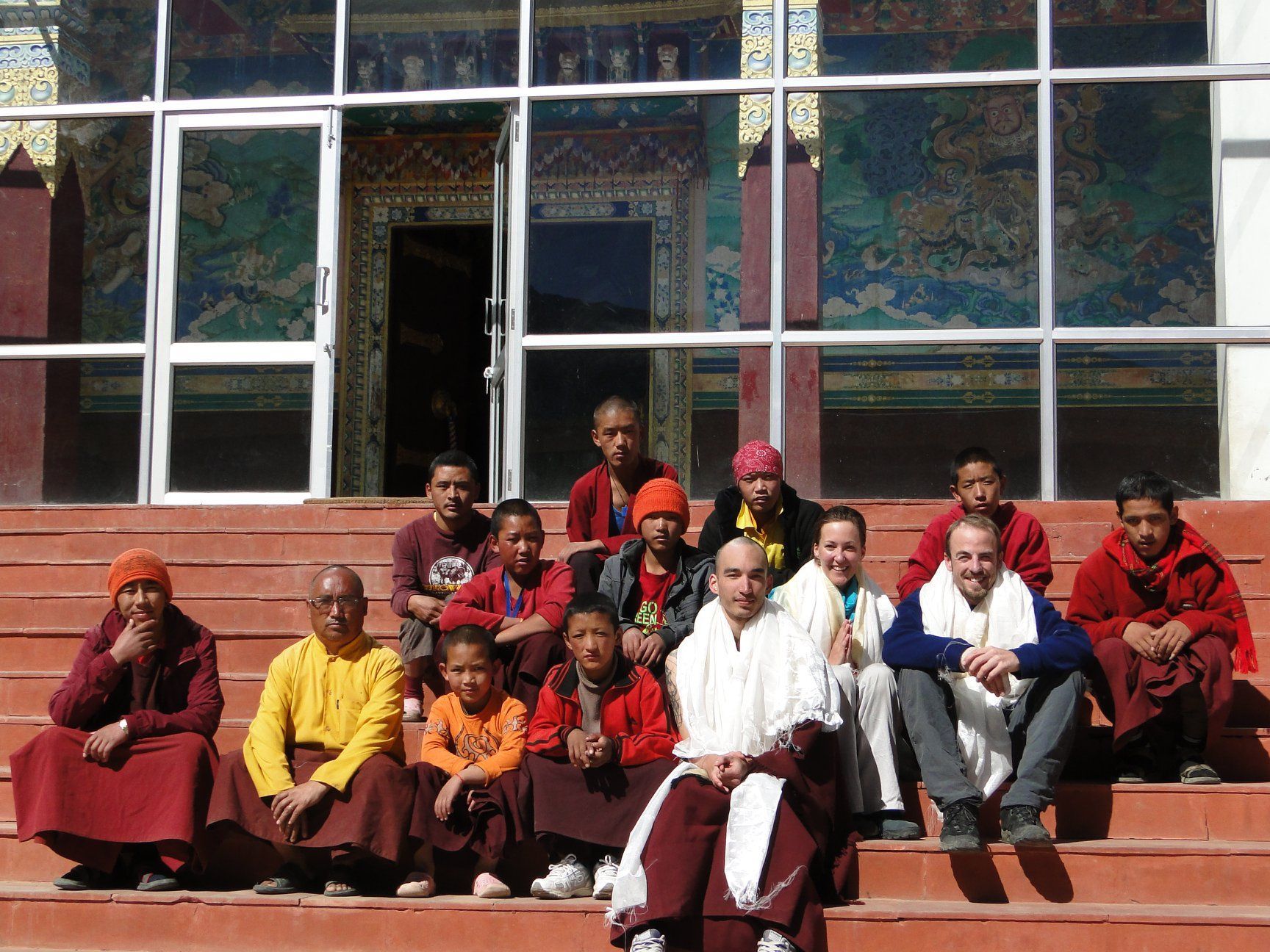 Group of people seated on steps outside a building, with colorful robes and a doorway behind them