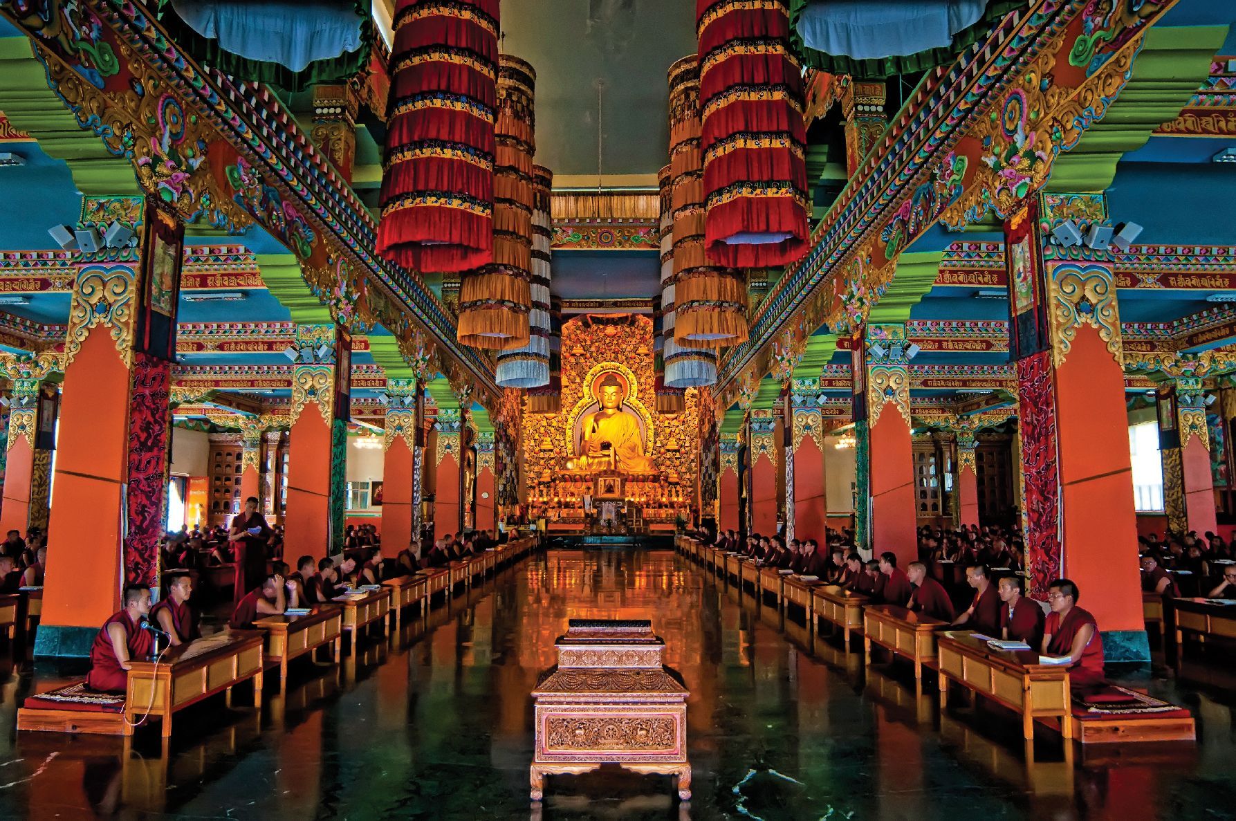 Colorful temple hall with rows of columns, hanging lanterns, and a reflective central water feature