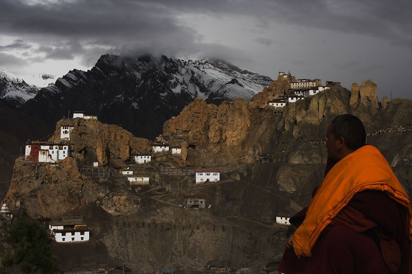 Monk in orange robe overlooking a mountain village at dusk