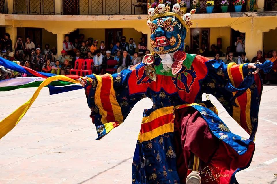 Masked dancer in colorful costume with flowing ribbons performing in a courtyard before a crowd