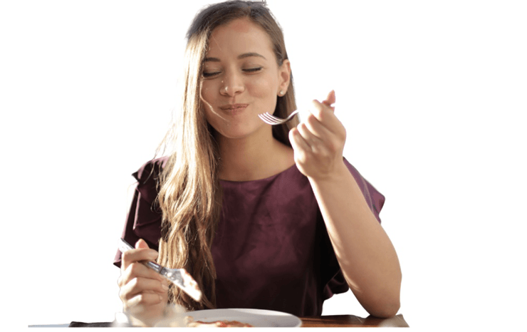 A woman is sitting at a table eating food with a fork.