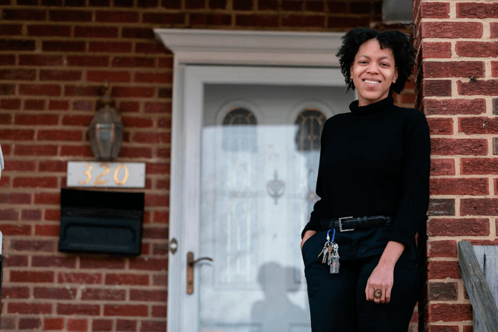 A woman is standing in front of a brick house holding keys.
