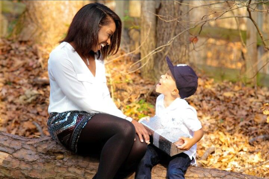 A woman and a child are sitting on a log in the woods.