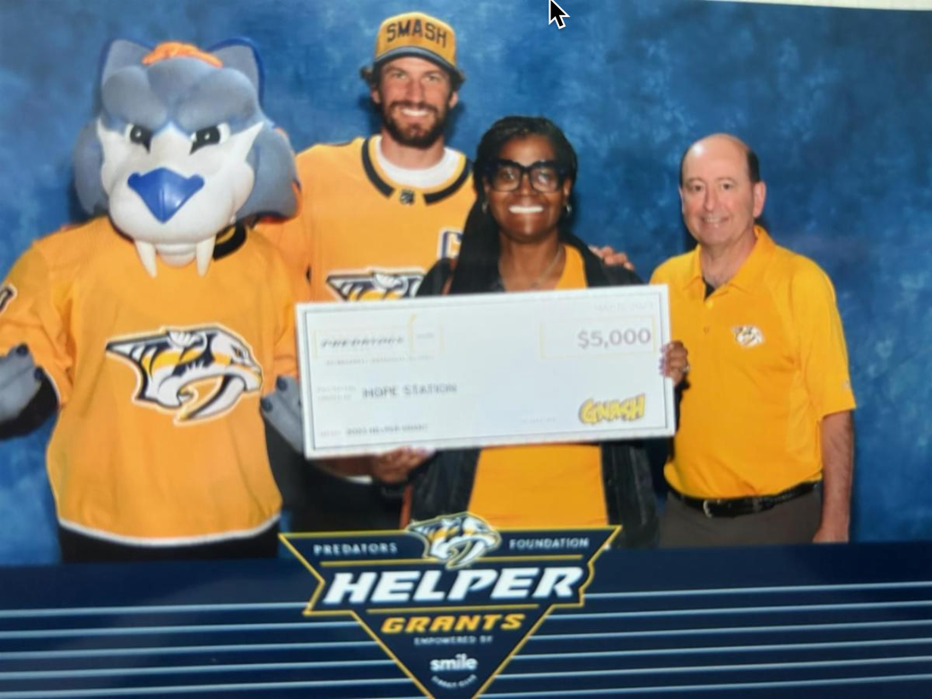 A woman holding a check in front of a helper grants sign