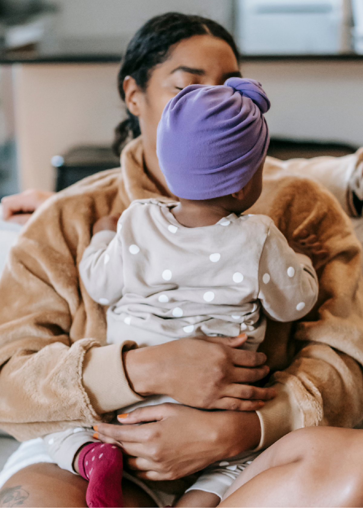 A woman is holding a baby wearing a purple turban.