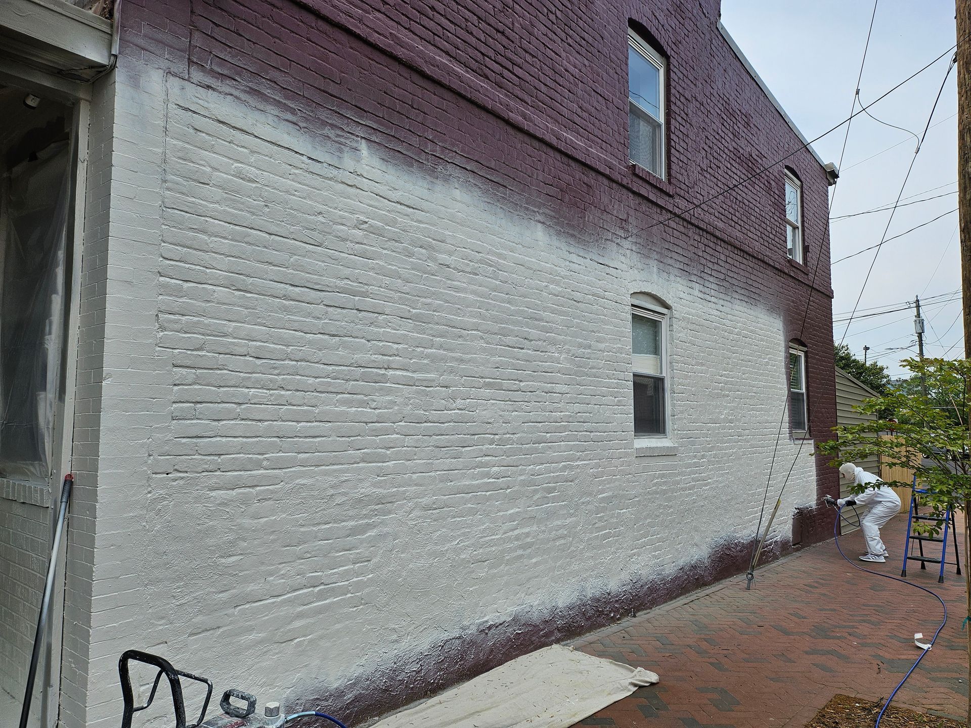 Person spraying white paint on a brick building. Exterior shot, partially painted, person in protective suit.