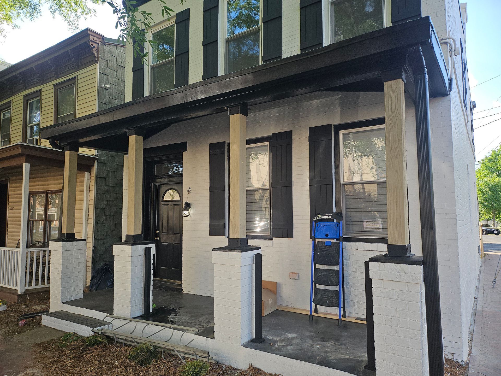 Two-story house with porch, painted black and white. A blue ladder sits on the porch.