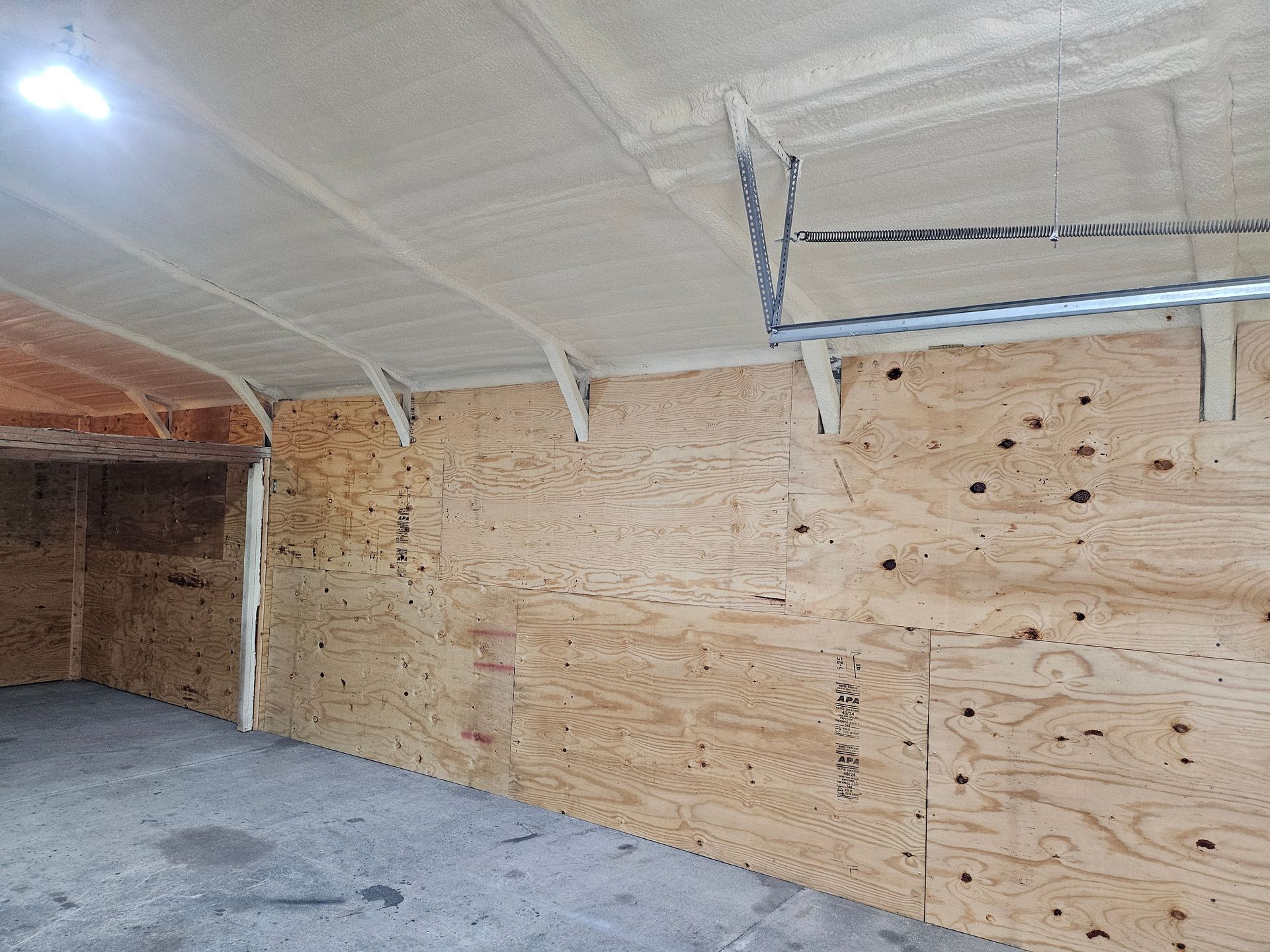 Plywood-paneled garage interior with spray foam insulation on the ceiling.