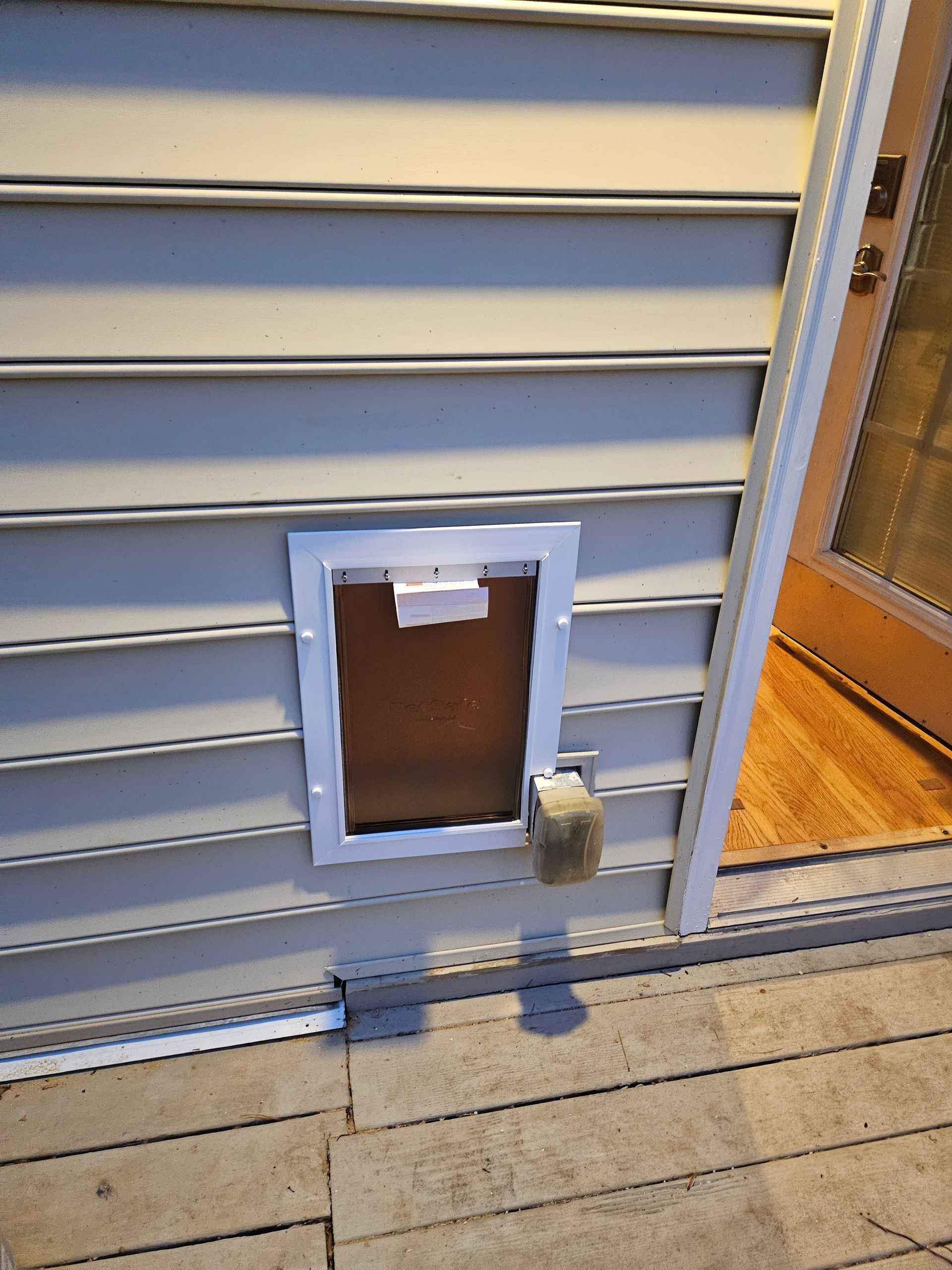 Pet door installed in gray siding beside an open door.