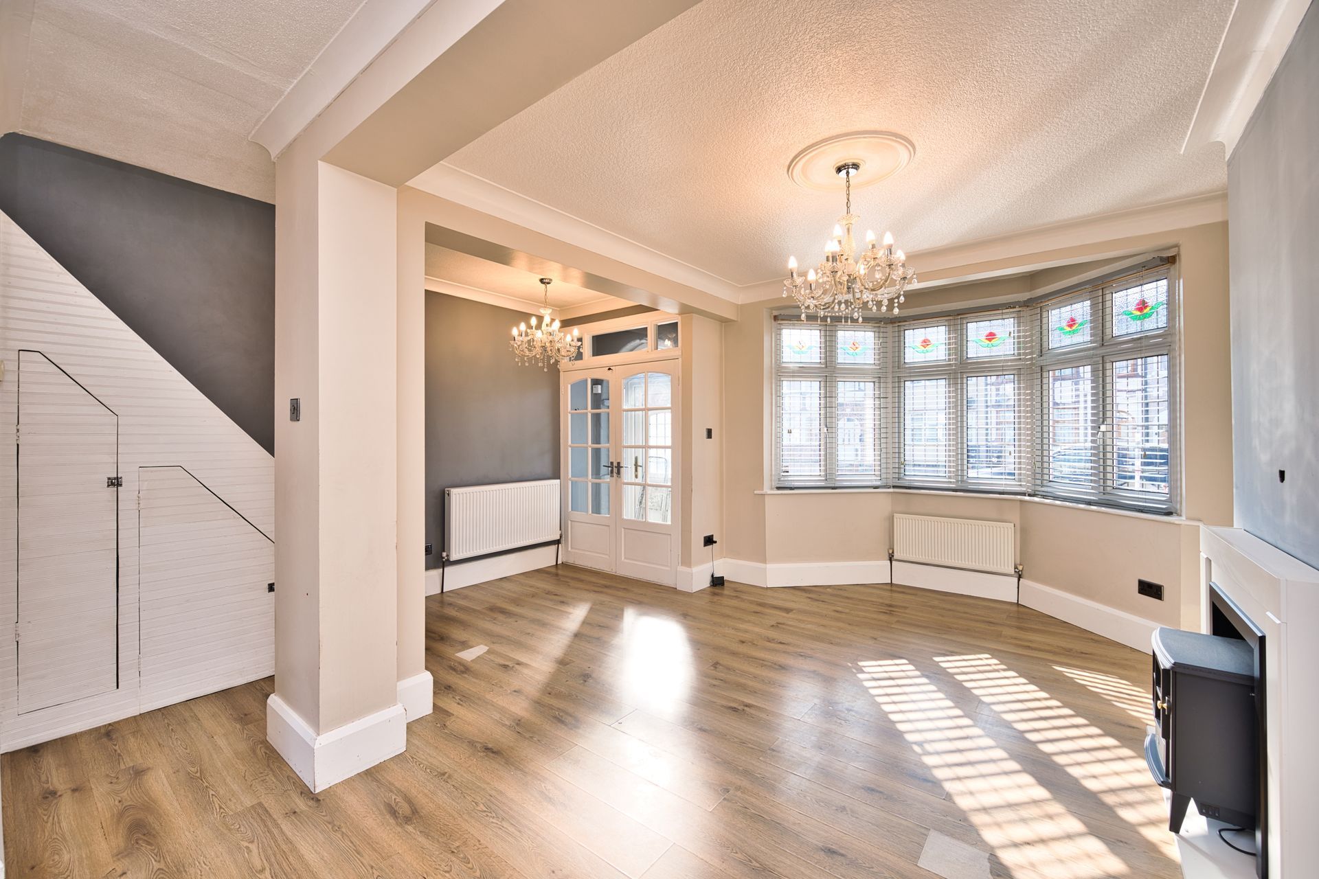 Bright empty living room with bay windows, chandelier, and sunlit wood floors