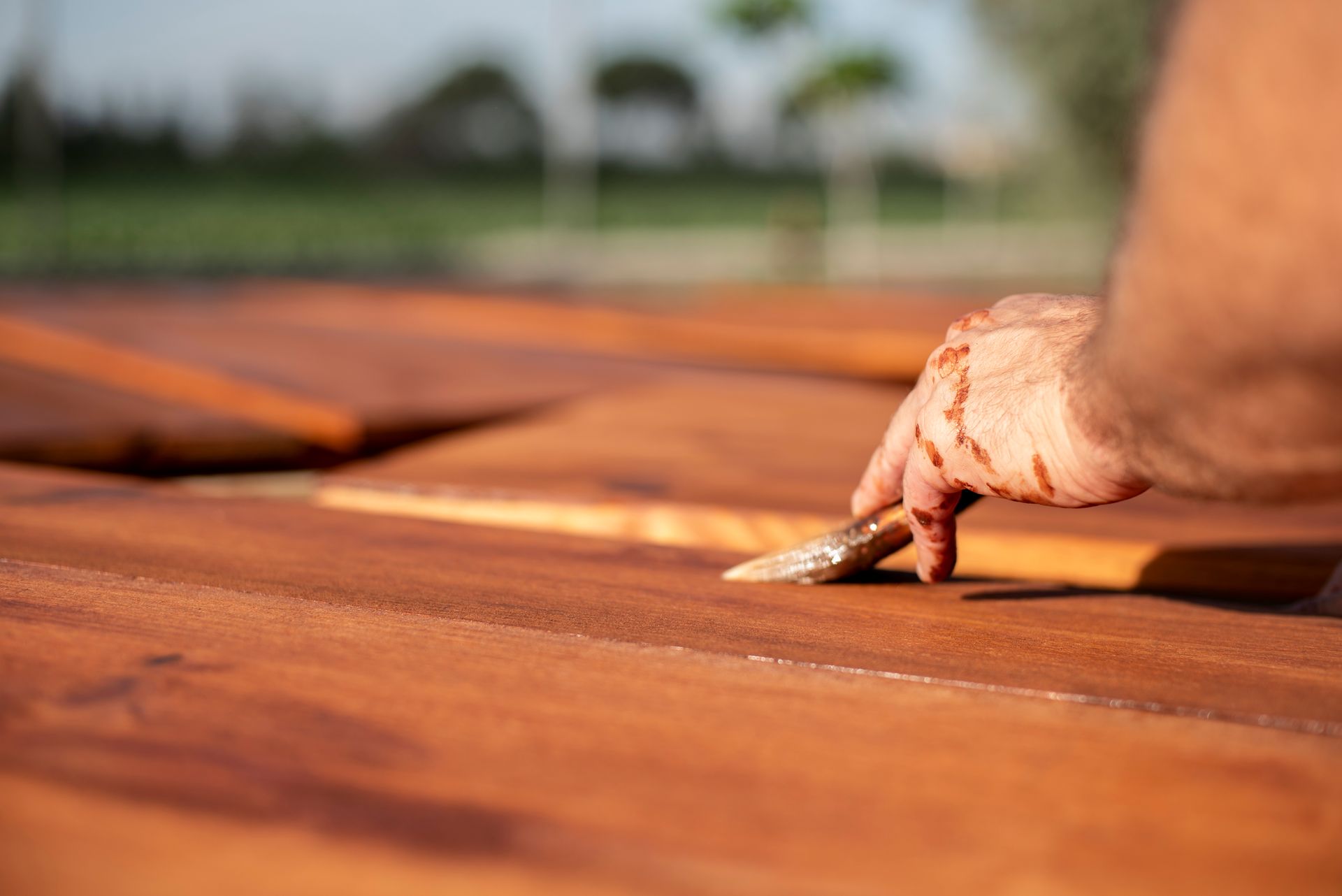Hand sanding a wooden deck board in warm sunlight
