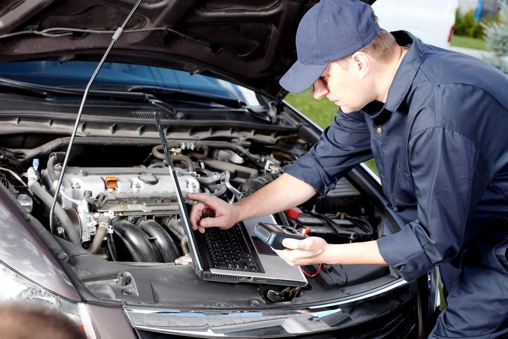 A Man Is Working On A Car Engine With A Laptop — Mechanic in Lismore, NSW