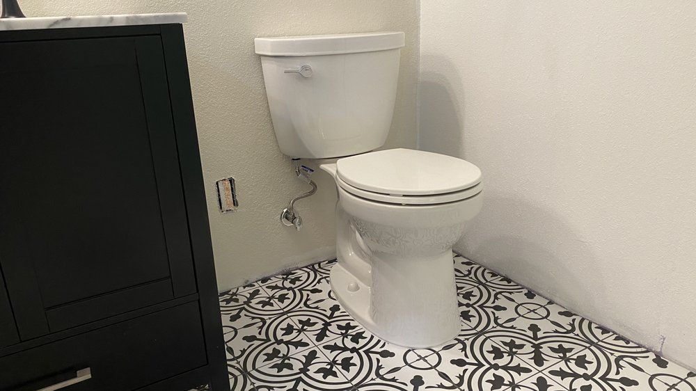 Small bathroom with a white toilet, black cabinet, and patterned black-and-white tile floor.