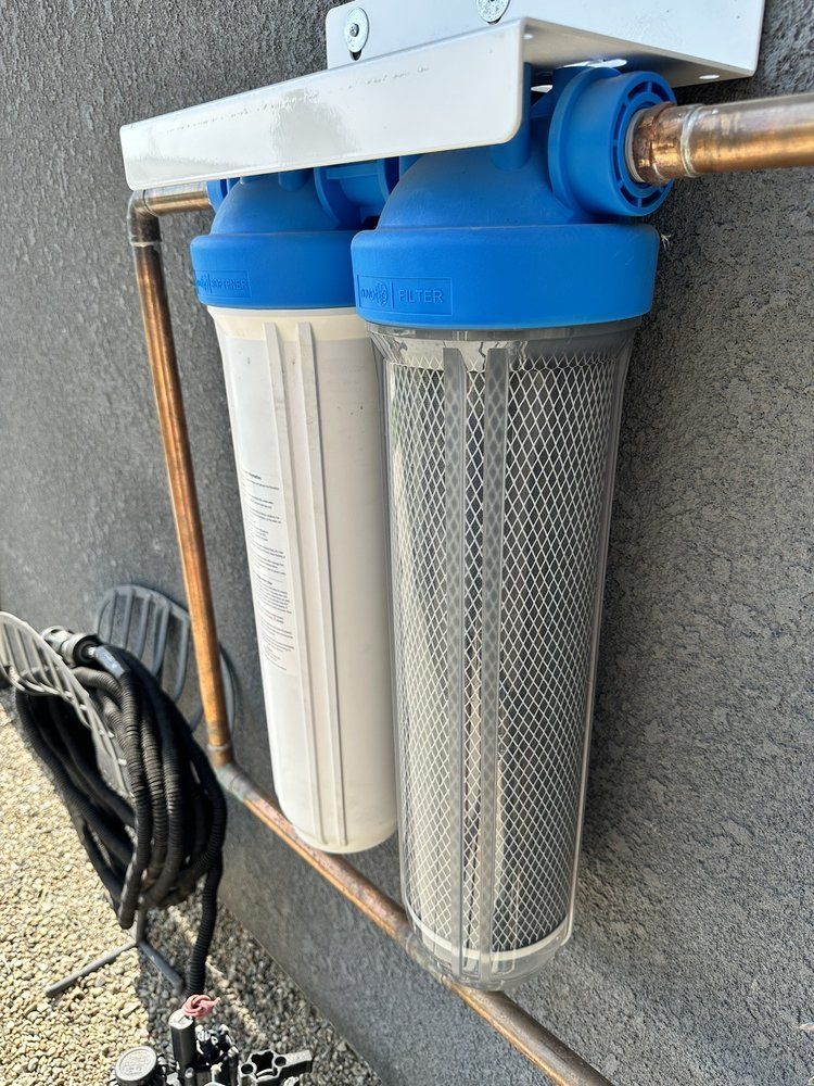 Wall-mounted water filtration system with blue and white filter cartridges and copper pipes.