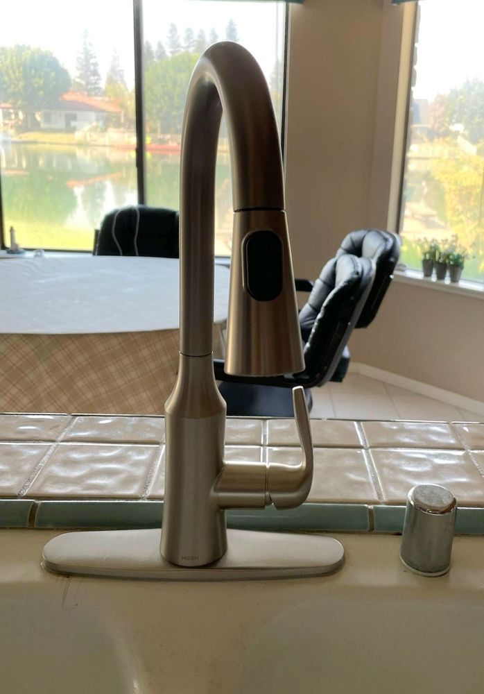 Chrome kitchen faucet at a sink with a soap dispenser and a lake view through the window.