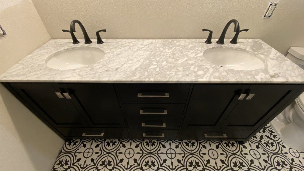 Black double vanity with white marble top, two sinks, and patterned tile floor in a bathroom.