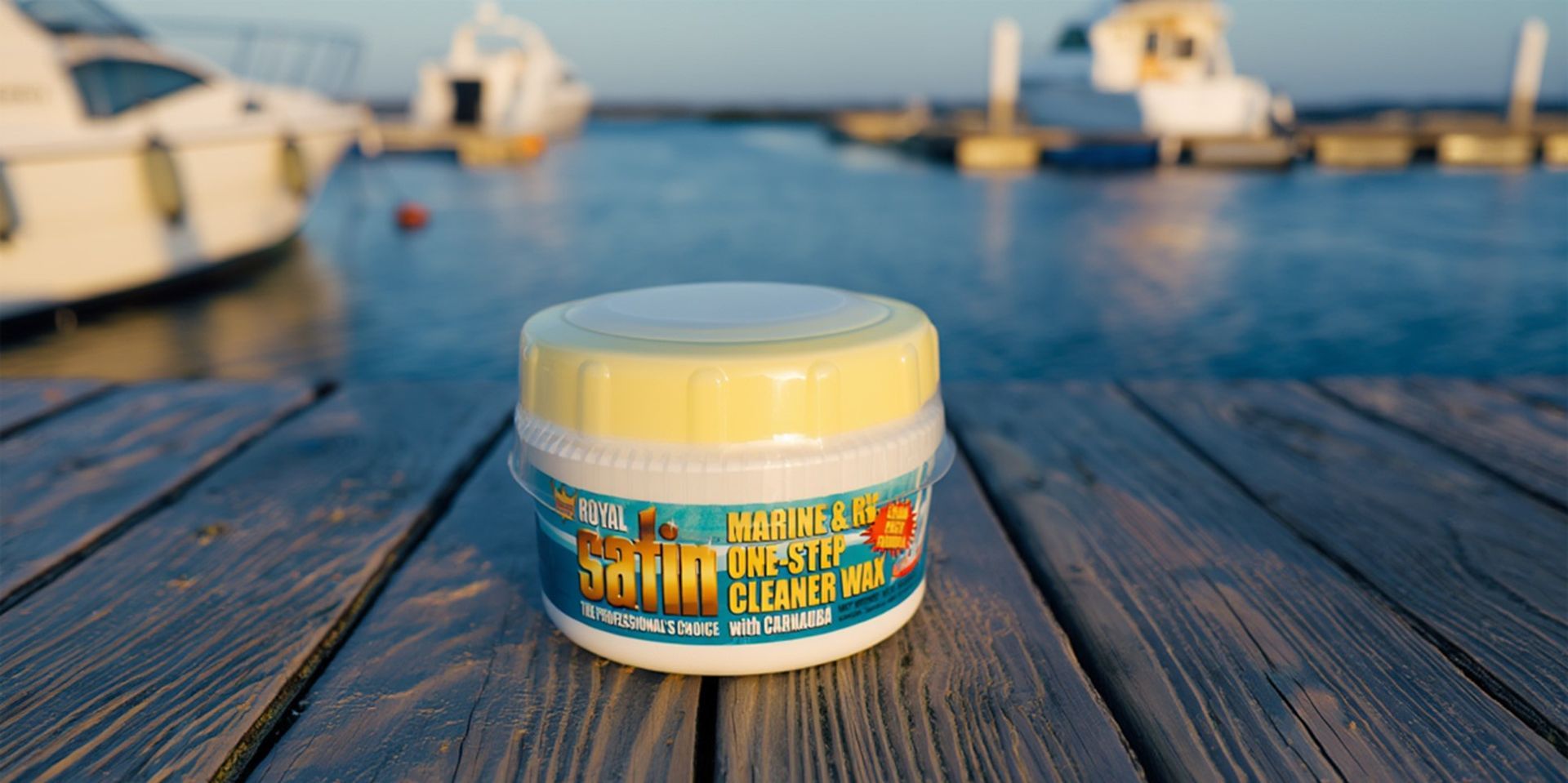Small cream jar with blue label on a wooden dock, with boats and water in the background