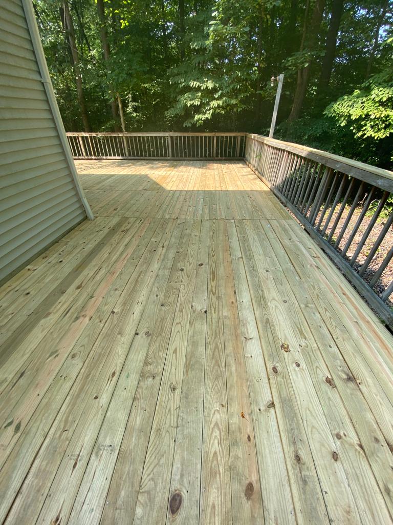 Wooden deck overlooking a wooded backyard, with railings and a house wall on the left.