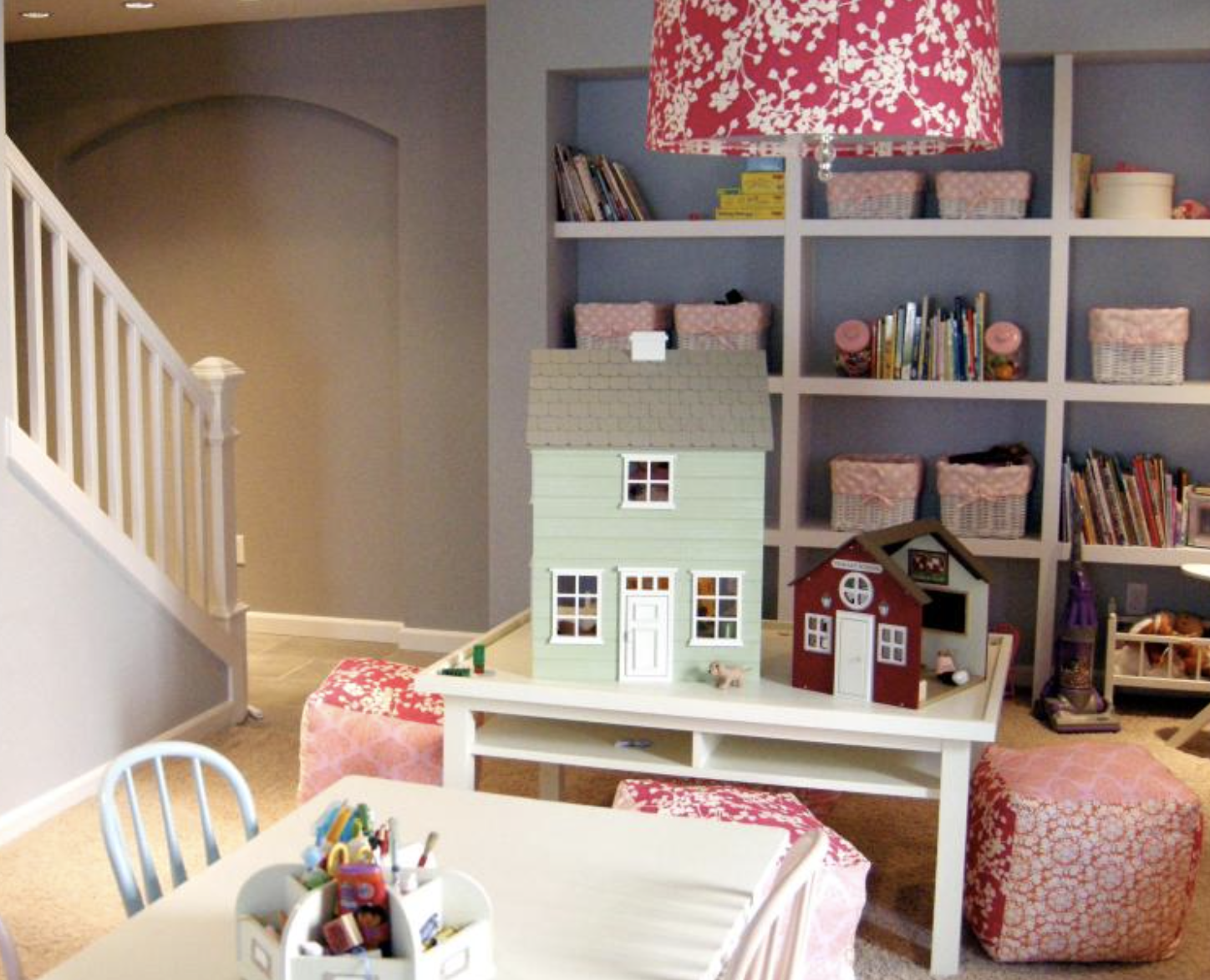 Playroom with dollhouse on a table, shelves of books, and pink patterned decor