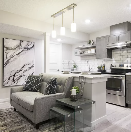 Modern open-plan living room and kitchen with gray sofa, white island, stainless appliances, and pendant lights
