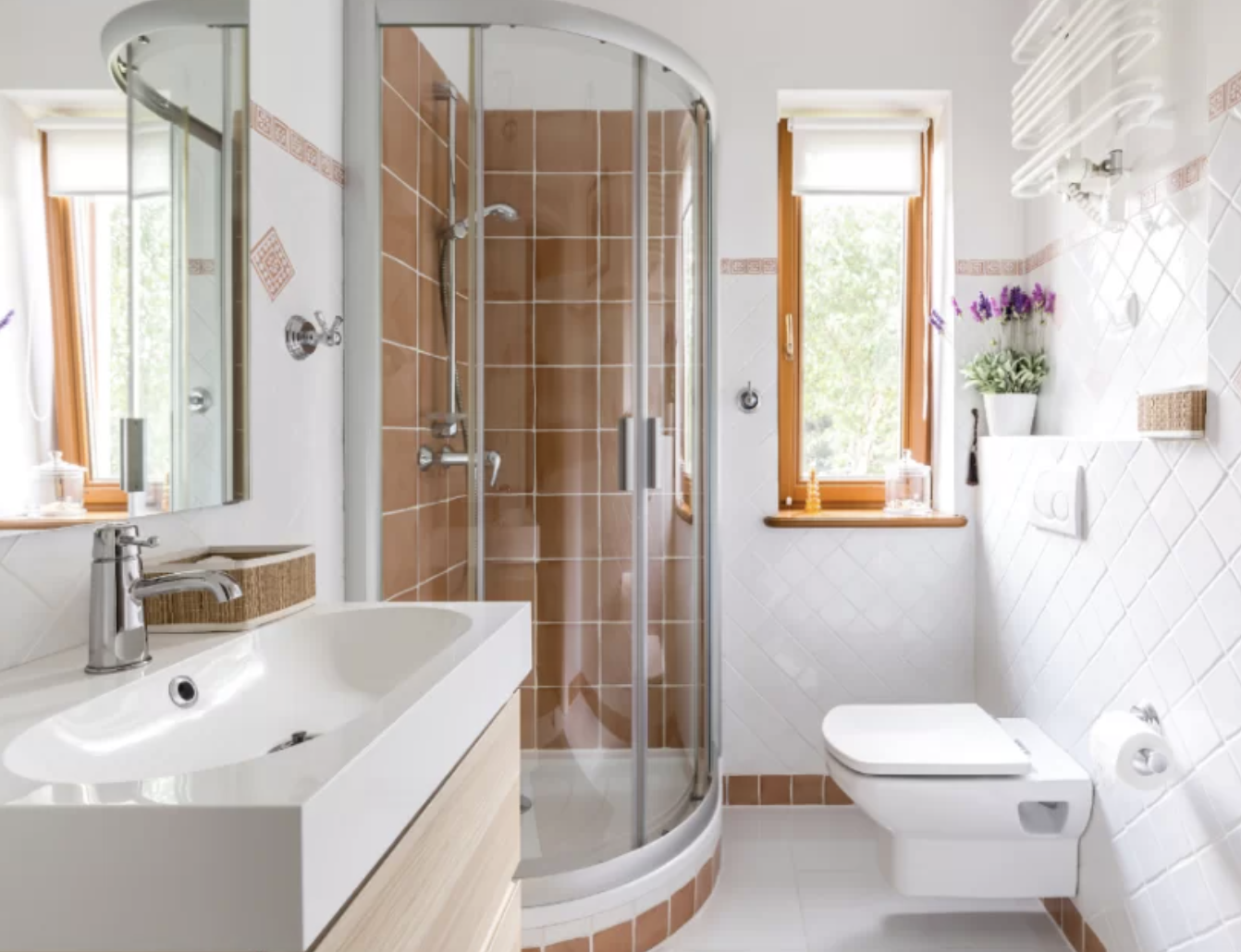 Bright modern bathroom with curved glass shower, sink, toilet, and white tile walls with wood-framed windows