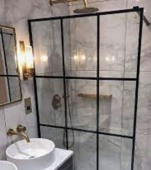 Bathroom with glass shower enclosure, white vessel sink, brass fixtures, and marble-pattern tile walls.
