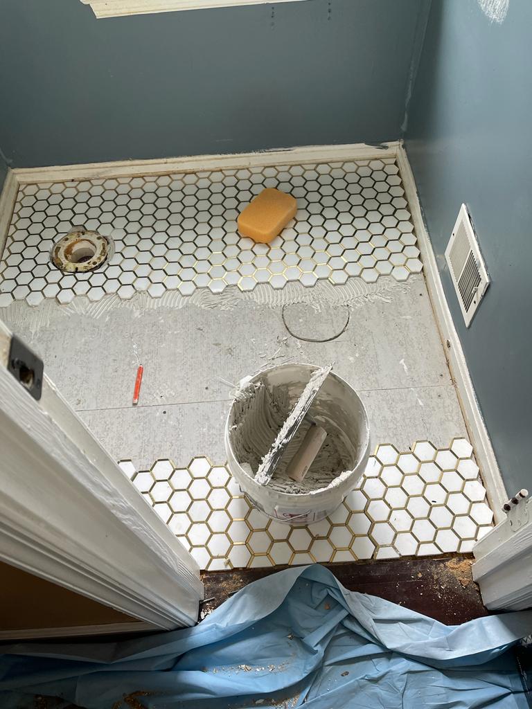 Tiled shower floor under construction with a drain opening, tools, and blue protective covering.