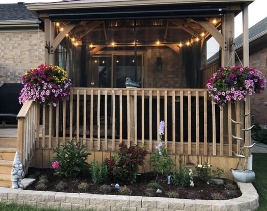 Front porch with wooden railing, hanging pink flowers, and warm lights on a brick house
