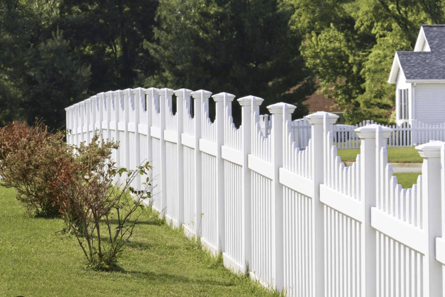 White picket fence curving along a green lawn with trees in the background