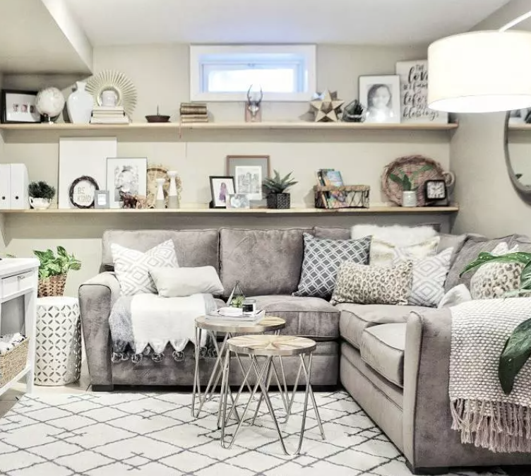 Cozy beige living room with sectional sofa, patterned pillows, floating shelves, and light rug