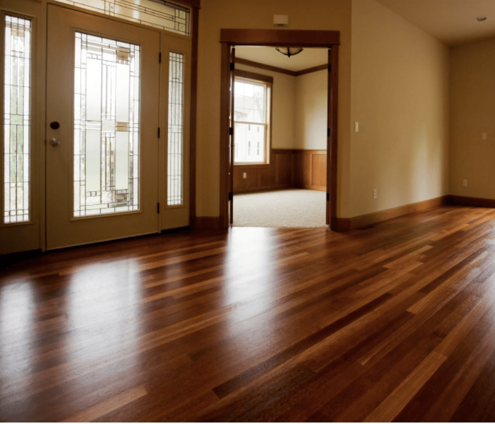 Empty room with polished hardwood floors and French doors opening to a brighter adjoining space