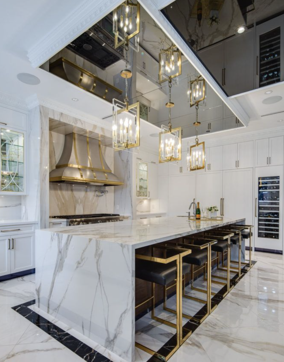 Modern white marble kitchen with gold pendant lights and a large island with black bar stools