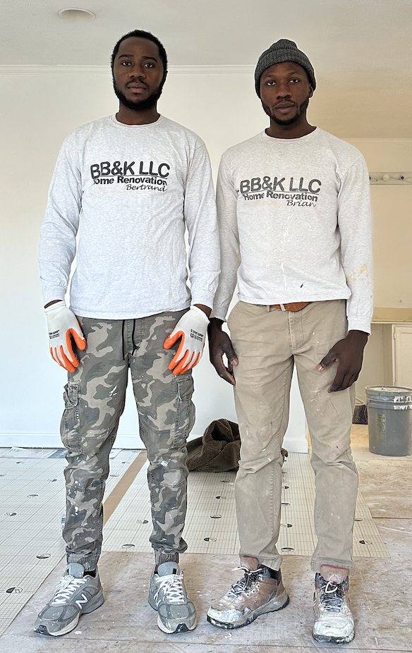 Two workers in a garage, wearing gloves and dusty clothes, standing side by side during a renovation.