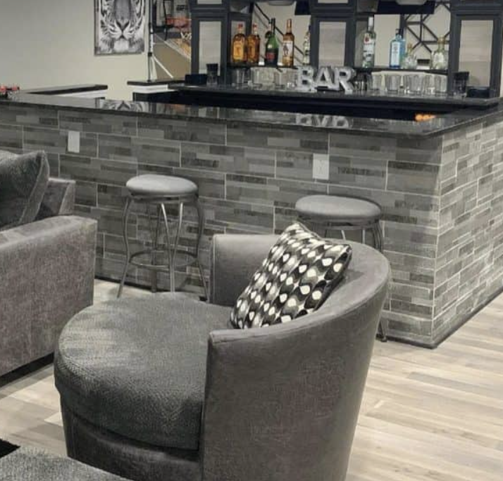 Modern gray home bar with stools, counter shelves, and a round chair in the foreground