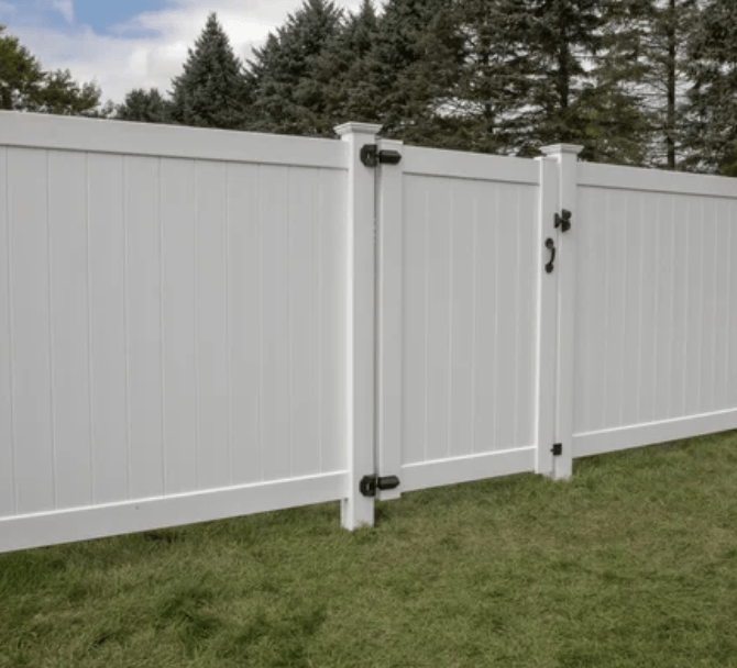 White vinyl fence with a matching gate in a grassy yard, with trees in the background