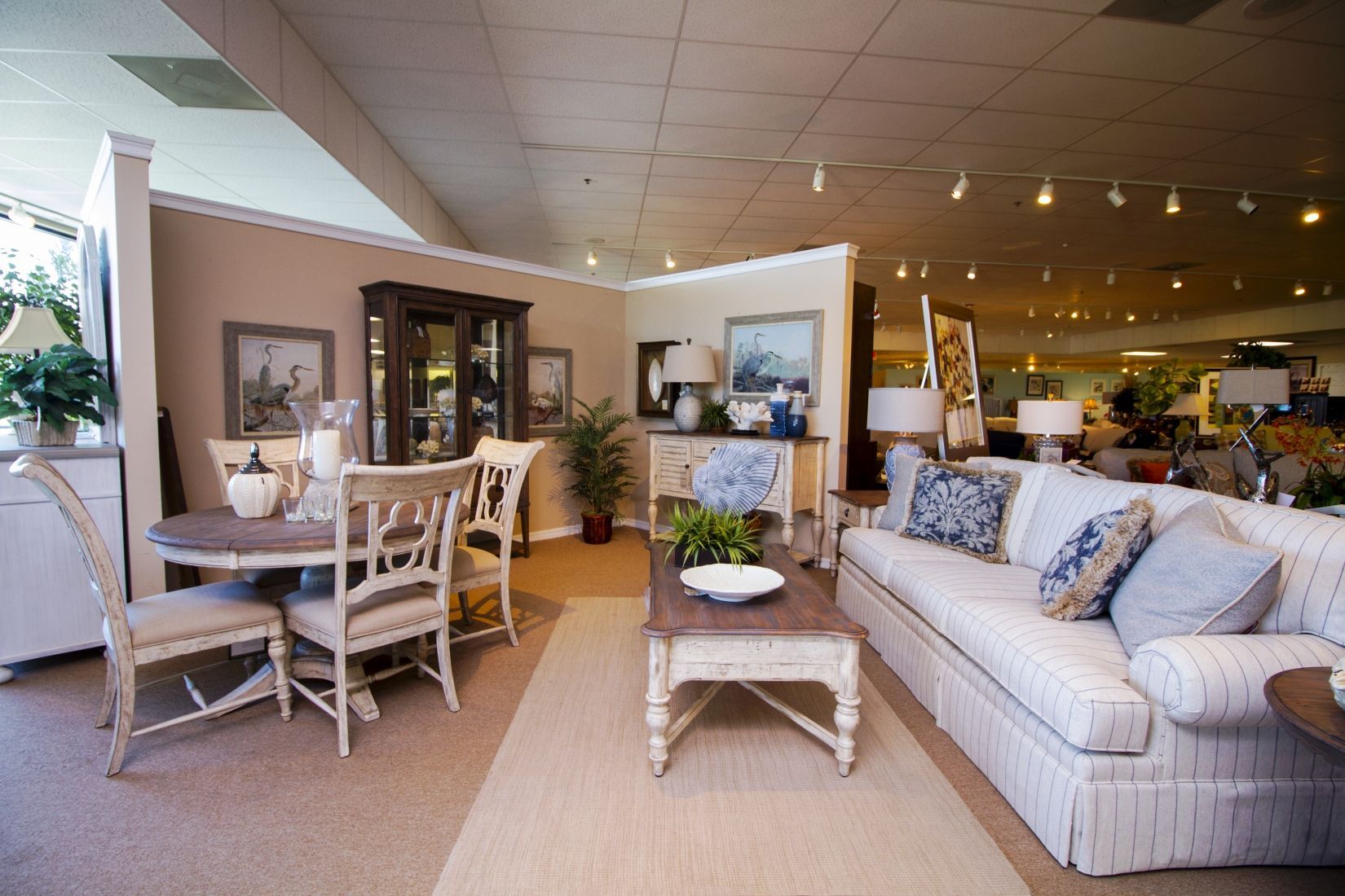 Bright furniture showroom with a sofa, dining set, coffee table, and warm lighting