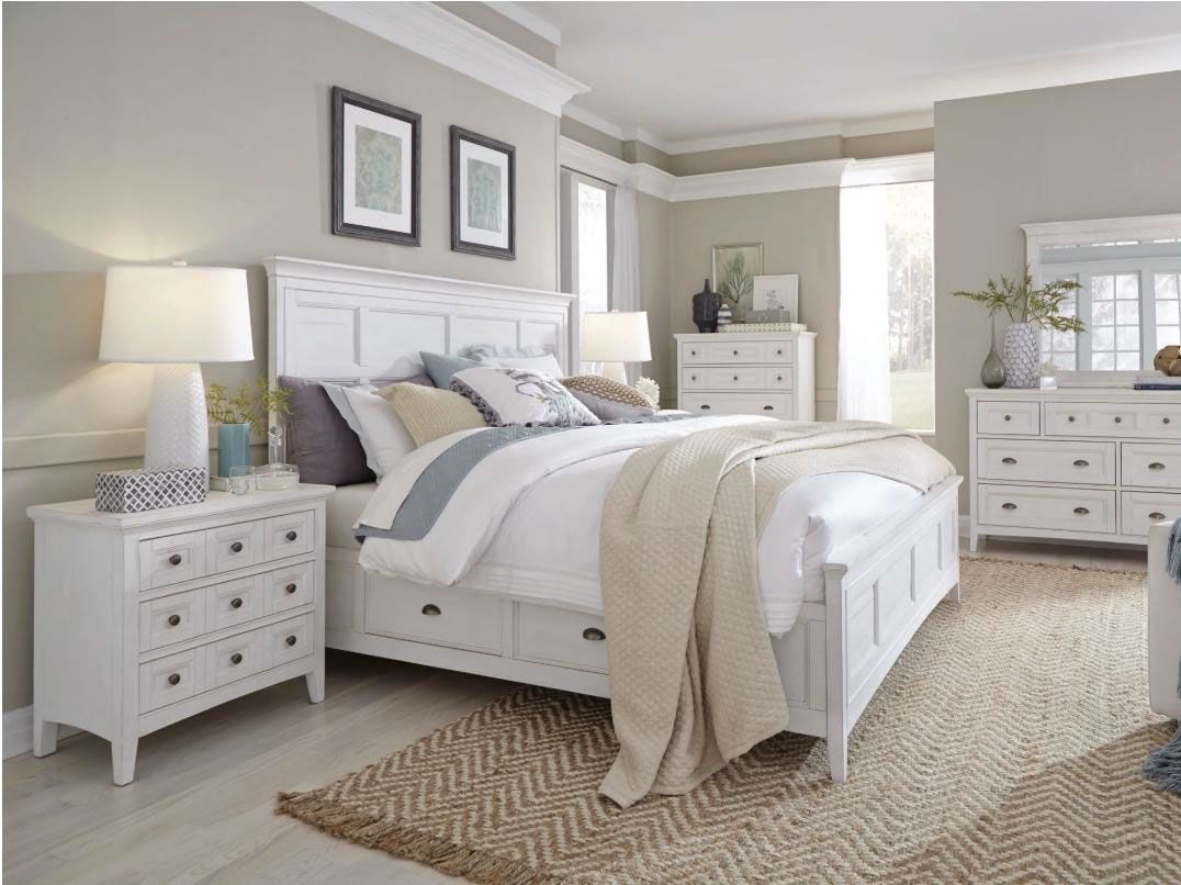 Bright bedroom with white bed, matching dressers, lamp, and beige rug in soft neutral tones