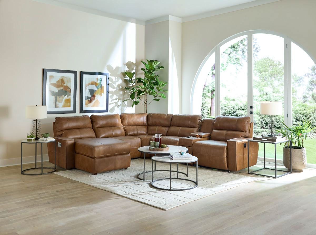 Bright living room with brown sectional sofa, round coffee table, framed art, plants, and large arched window.