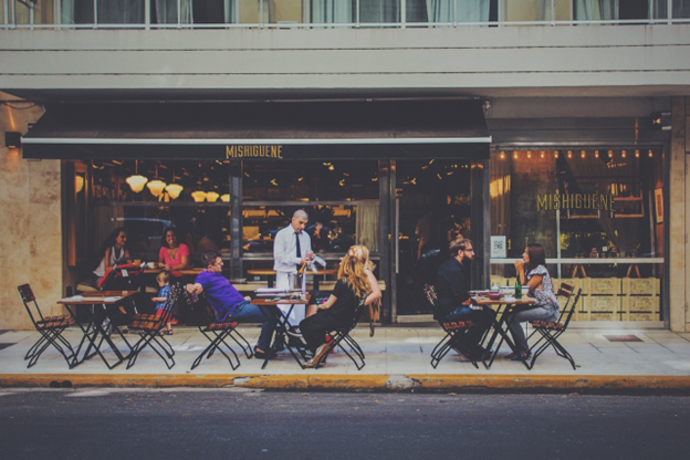 A group of people are sitting at tables outside of a restaurant.