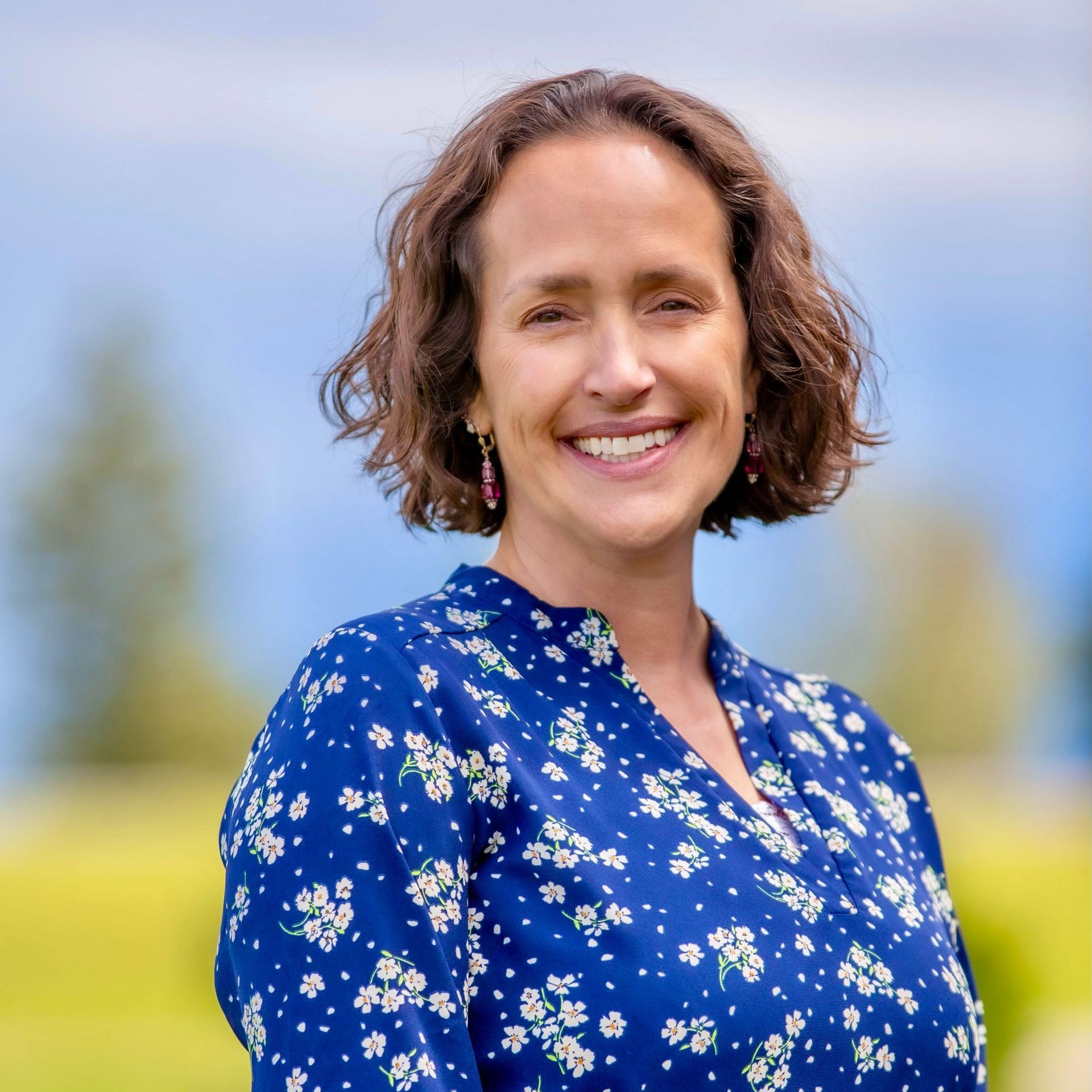 A woman in a blue floral shirt is smiling for the camera.