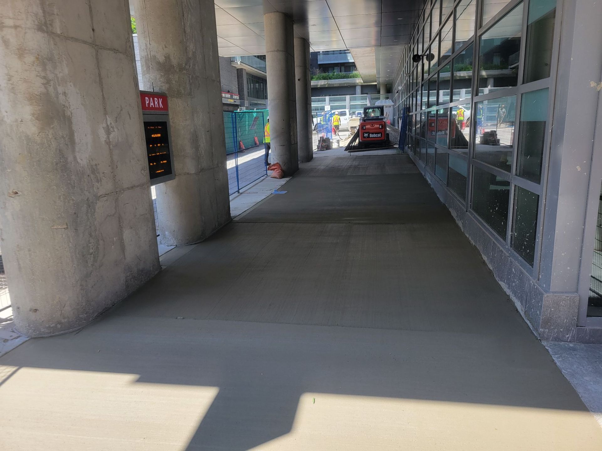 A concrete walkway between two buildings with cars parked in the background.