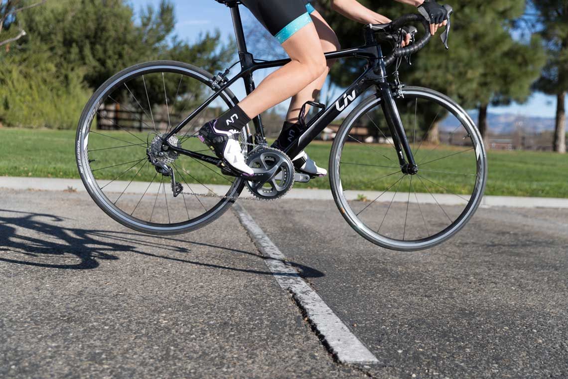Cyclist on a black road bike rides over a painted road line outdoors on a sunny day.
