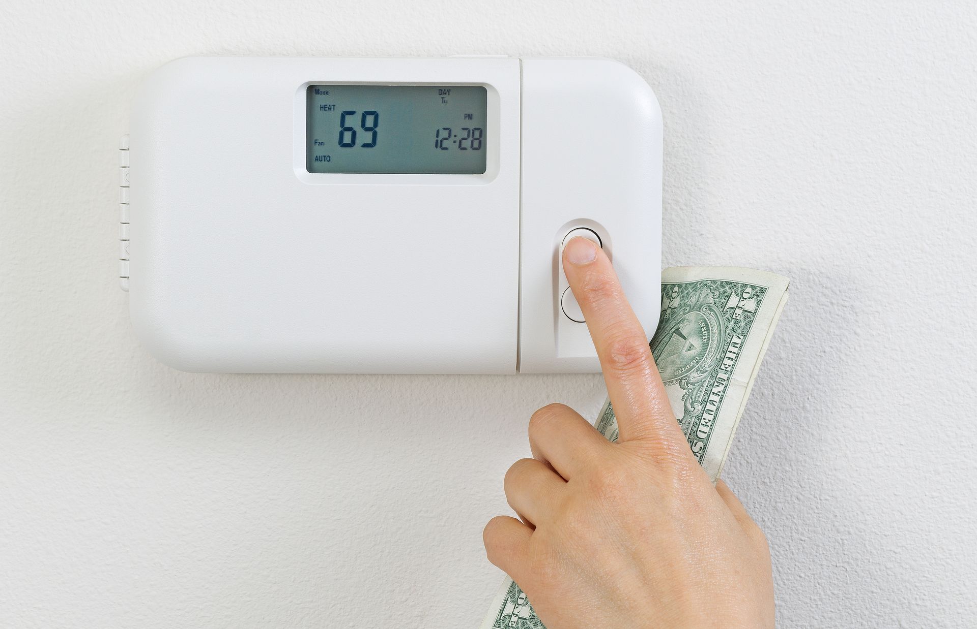 Hand pressing thermostat button with money, representing high energy costs.