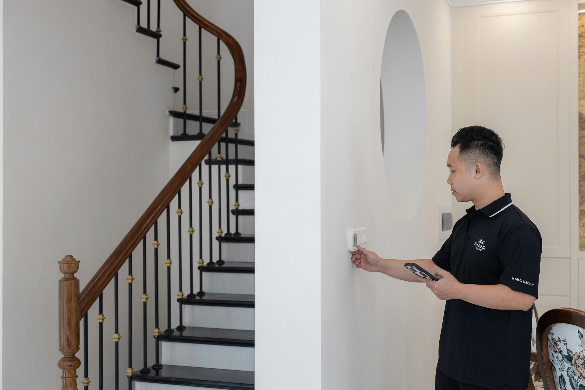 Man inspecting a light switch on a white wall near a wooden staircase.