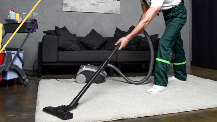 A man is using a vacuum cleaner to clean a rug in a living room.