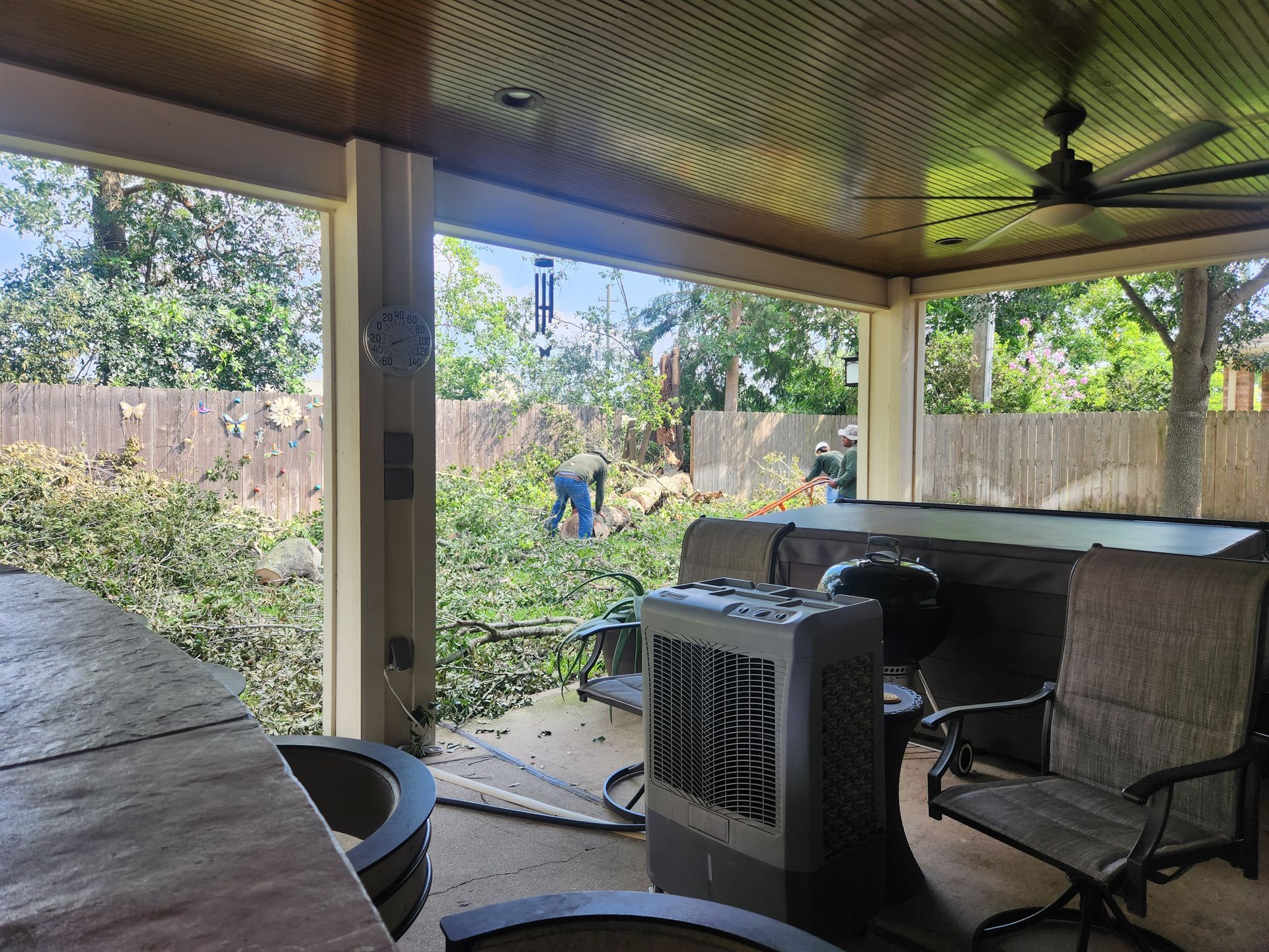 Covered patio with outdoor furniture, a heater, and a person working in a leafy backyard.