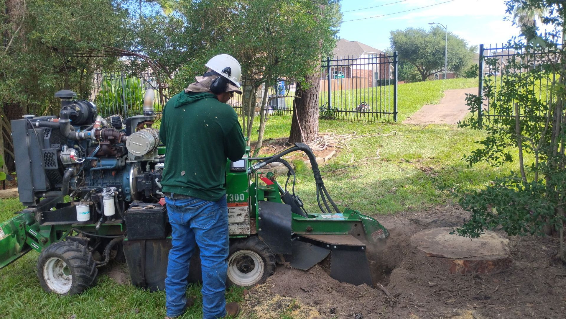 Worker operating a small excavator beside a dirt path, clearing soil near a fence and trees.